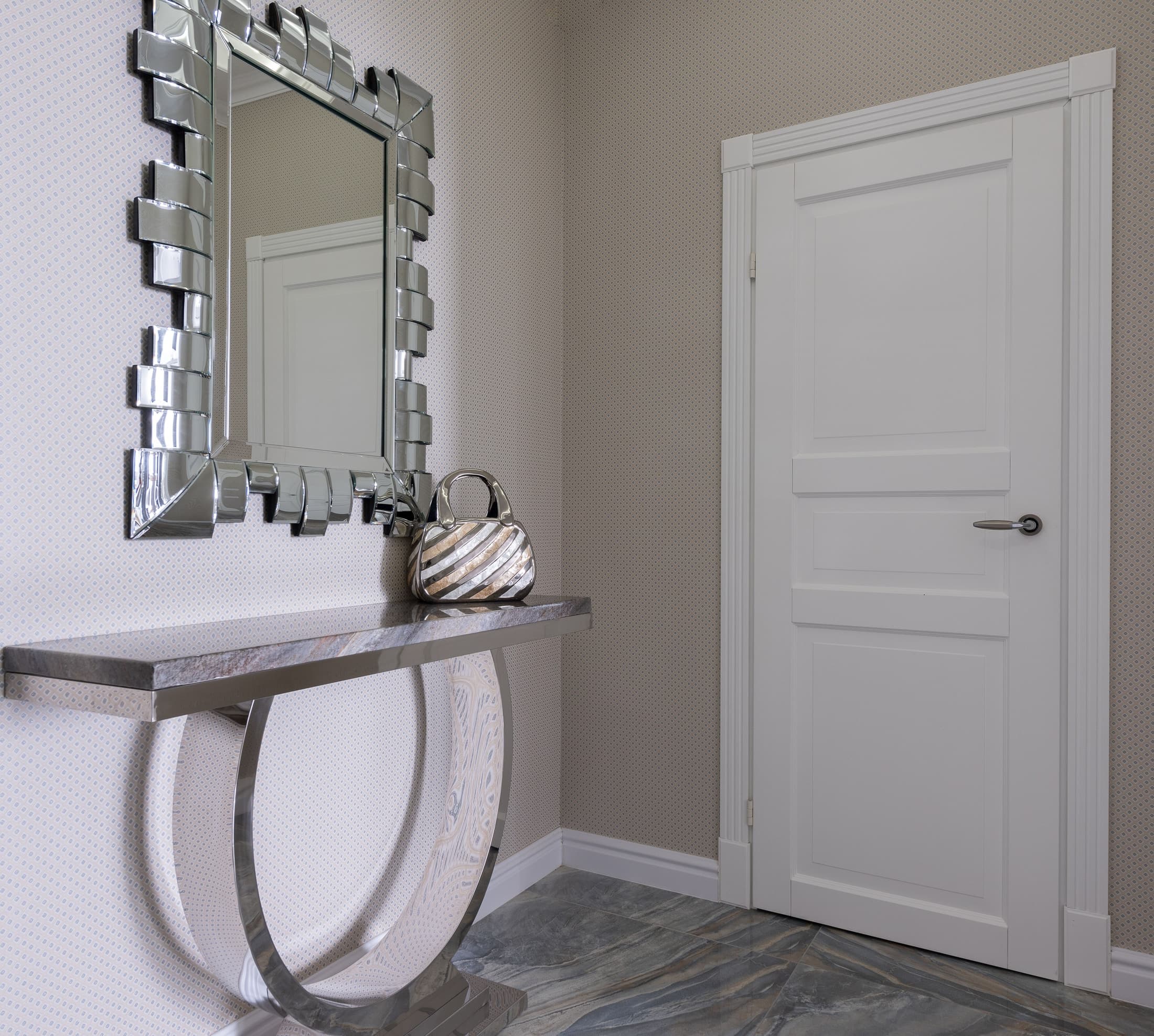 An elaborate mirrored border above a narrow console, reflecting a white door against patterned walls.