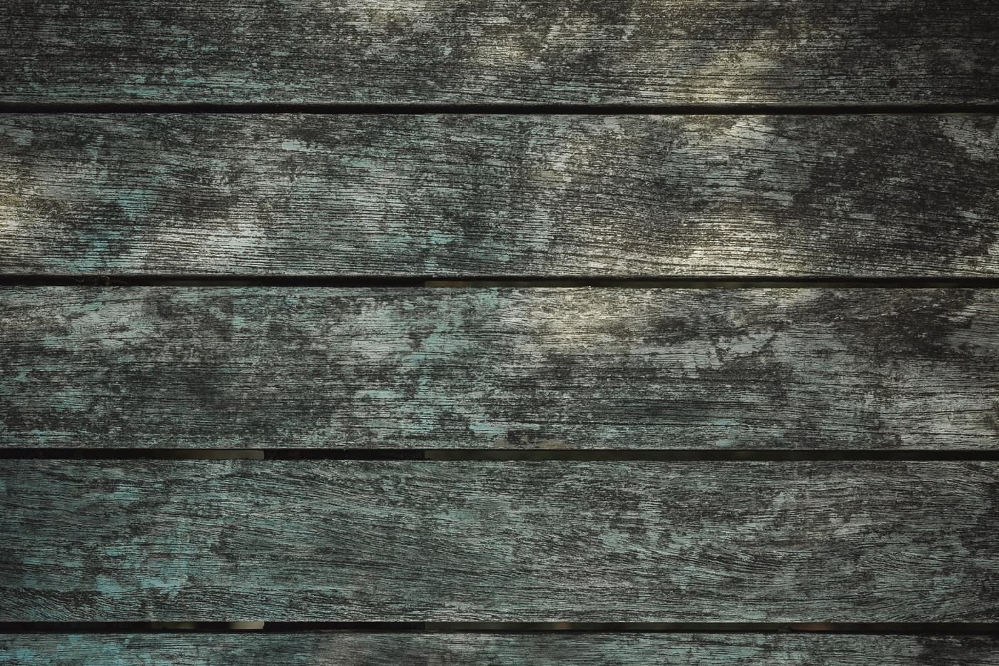 Weathered timber boards show dark grain, gaps and patches of faded green.