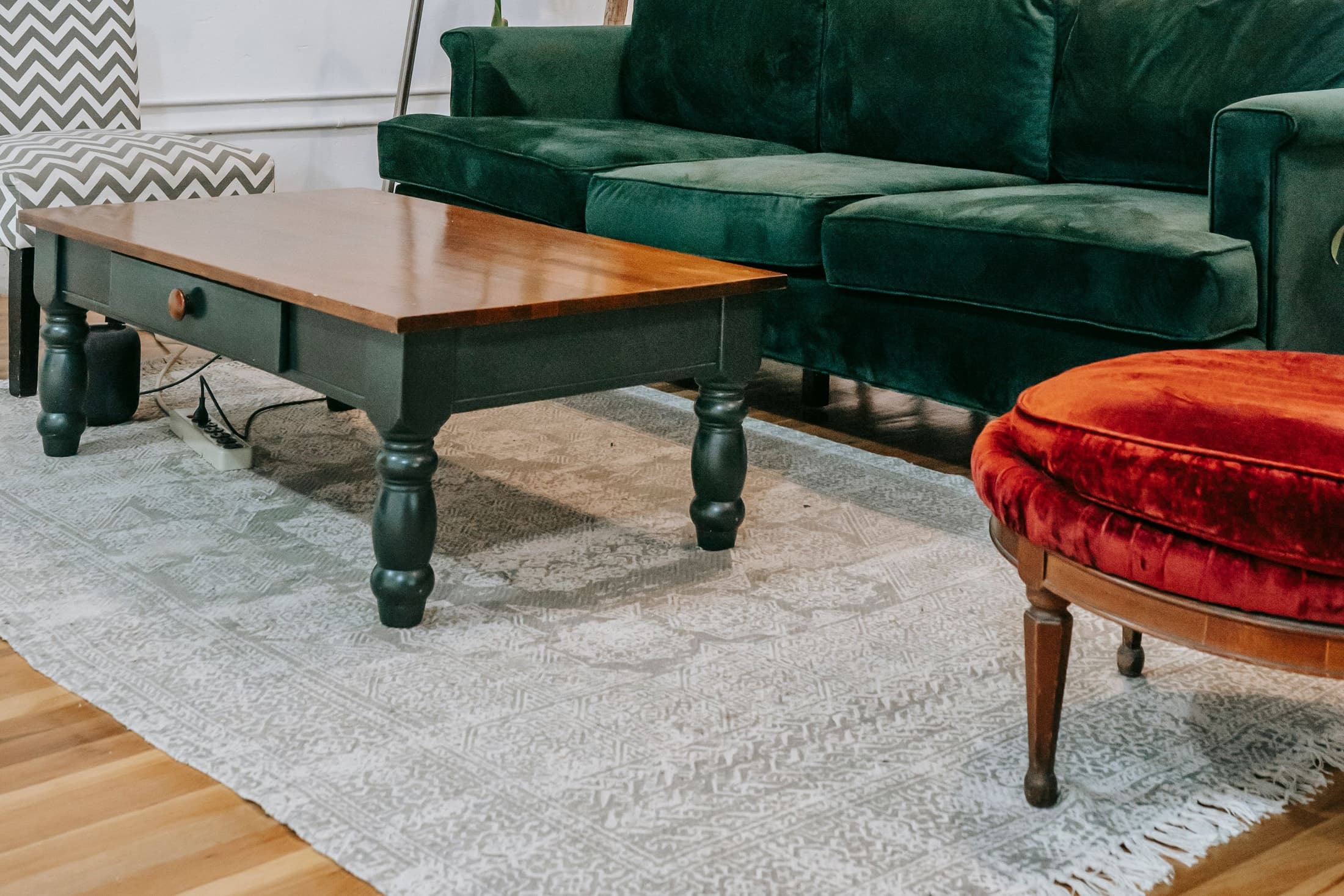 A pale patterned rug beneath a timber-topped low table and red stool, beside a green sofa and chevron chair.