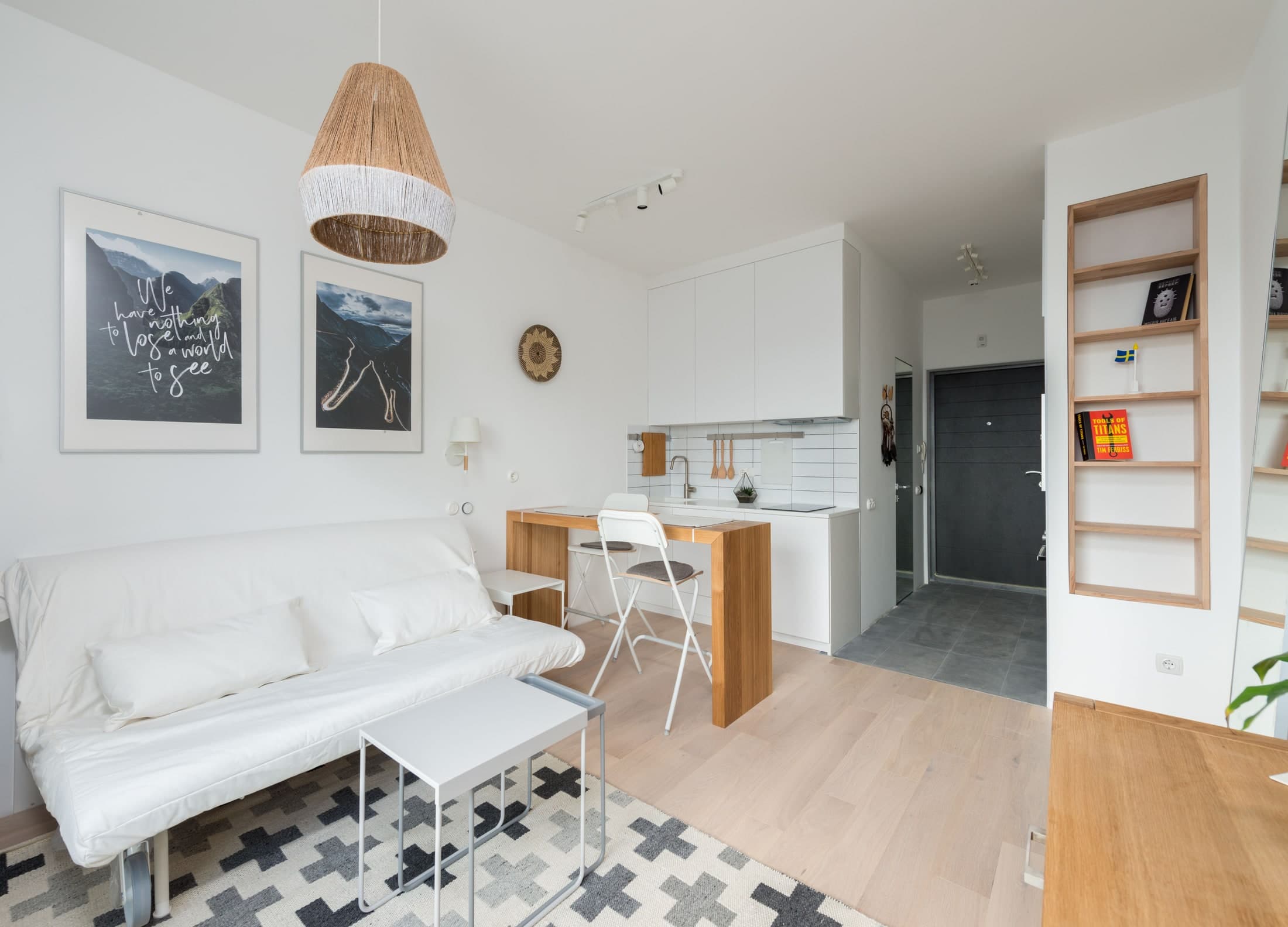 A timber counter with two white seats stands between a white kitchen and a sofa, with a low coffee table in front.
