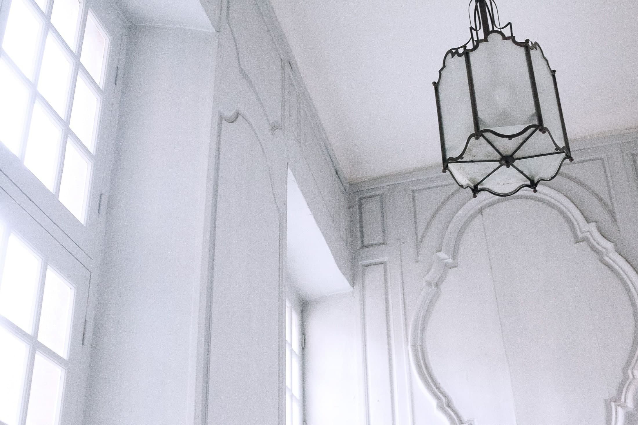 Daylight falls across white moulded walls and window framing, beneath a dark-framed hanging lantern.